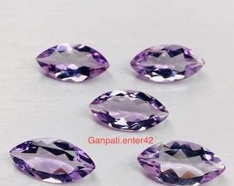May include: Five marquise-shaped amethyst gemstones, each with a purple hue and a faceted cut. The gemstones are arranged in a semi-circle on a white surface.