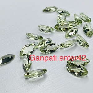 May include: A collection of light green marquise-shaped gemstones. The gemstones are scattered on a white surface.