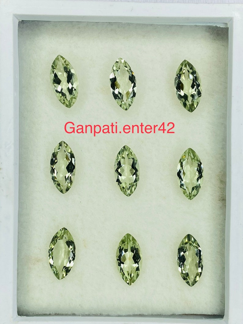 May include: Eight marquise-shaped green gemstones displayed in a white box. The gemstones are arranged in three rows of two. The text "Ganpati.enter42" is printed in red on the box.