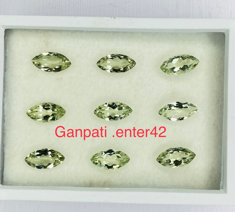 May include: Eight marquise-shaped green gemstones displayed in a white box. The gemstones are arranged in two rows of four. The text "Ganpati.enter42" is printed in red on the bottom of the box.