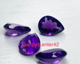 May include: Four pear-shaped amethyst gemstones, each with a deep purple hue and a faceted cut, are arranged on a white surface.