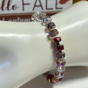 Könnte beinhalten: Ein Armband aus schimmernden Glasperlen in den Farben Klar, Rosa und Lila. Die Perlen sind facettiert und haben ein schimmerndes Finish.