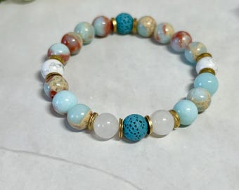 May include: A beaded bracelet with blue, white, and brown stones. The bracelet has a gold accent and a lava rock bead.