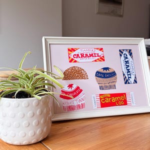 May include: A white framed print on a light pink background featuring illustrations of Tunnock's confectionery products including Caramel Wafer Biscuit, Caramel Log, and various chocolate-covered treats with visible brand text and logos.
