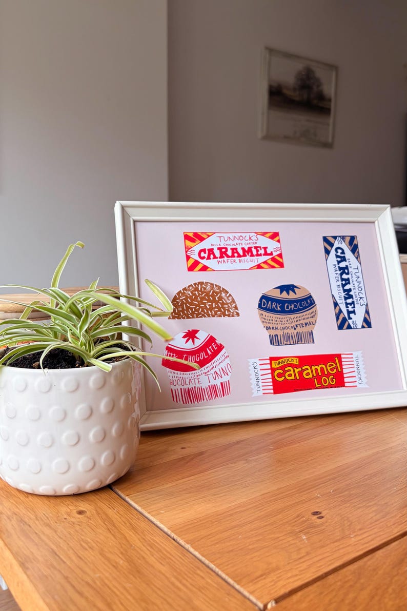 May include: A white framed print on a light pink background featuring illustrations of Tunnock's confectionery products including Caramel Wafer Biscuit, Caramel Log, and various chocolate-covered treats with visible brand text and logos.