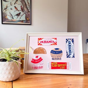 May include: A framed print on a light pink background featuring illustrations of Tunnock's confectionery products, including a Caramel Wafer Biscuit, a Caramel Log, and various chocolate-covered treats with red, blue, and white branding.