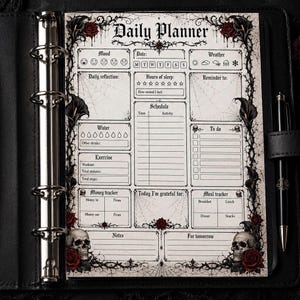 May include: A black daily planner with a gothic theme. The planner features a detailed layout with sections for mood, date, weather, and daily reflection. Decorative elements include roses, skulls, and spiderwebs. A pen is visible on the right side.