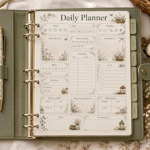 Puede incluir: Una agenda diaria de anillas en color verde salvia con un mecanismo de metal dorado y un bolígrafo a juego con estampado floral. La página de la agenda incluye secciones para el estado de ánimo, el tiempo, el horario, tareas, agua, ejercicio y notas.