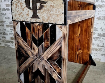Op de afbeelding: Een houten paardensprong met een zwart-wit geometrisch patroon aan de voorkant. De bovenkant van de sprong is bedekt met een wit en bruin koeienhuid met een zwart "CF" monogram.