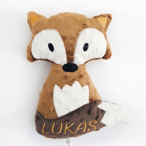 May include: Brown plush fox stuffed animal with white accents and black eyes. The fox has a white belly and a brown tail with the name "Lukas" embroidered in gold thread.