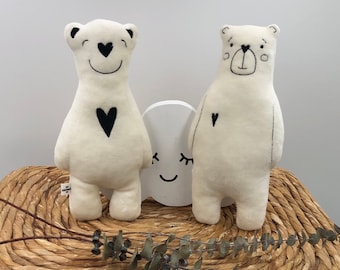 May include: Two plush polar bear toys with black heart and face details. One bear has a smiling face and a heart on its chest. The other bear has a heart on its chest and a neutral expression. A white cloud-shaped decoration is behind the bears.