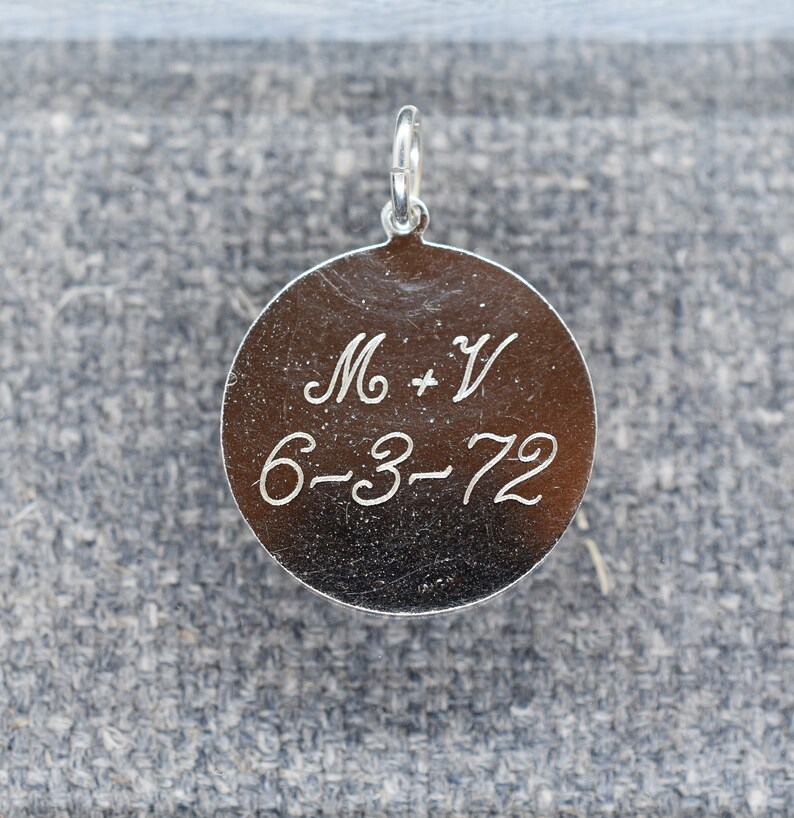 May include: Silver round charm with the inscription "M + V 6-3-72" engraved on the front.