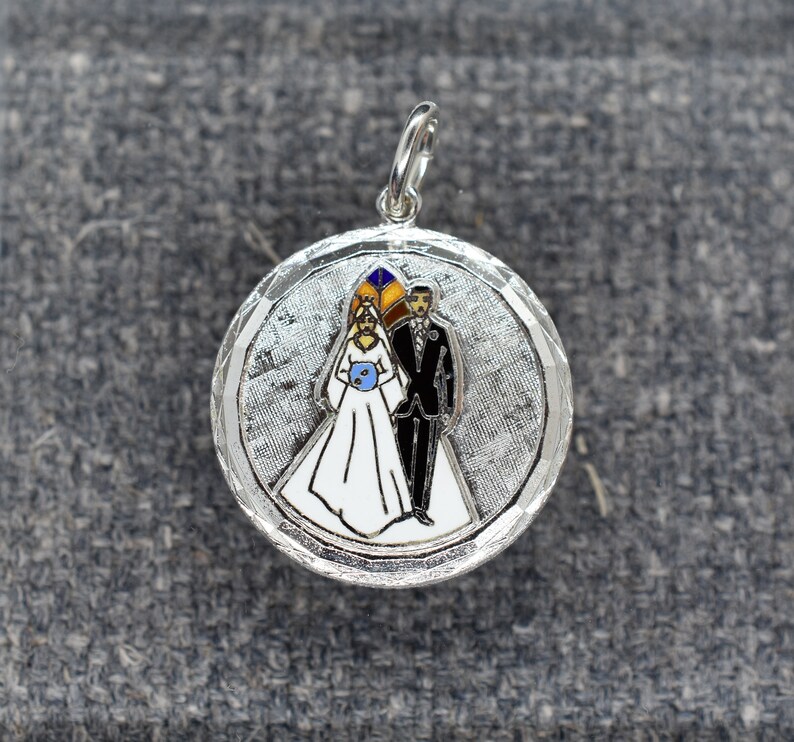 May include: Silver charm with a white enamel bride and groom in a wedding ceremony. The charm has a textured silver background.