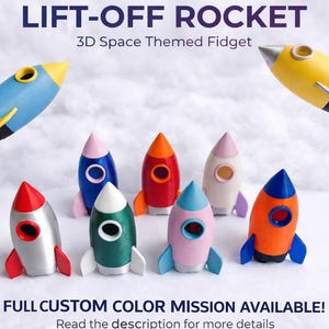 May include: A collection of colorful 3D-printed rocket ship fidget toys. The rockets are in various colors, including blue, yellow, red, pink, and orange. The image includes the text "LIFT-OFF ROCKET" and "3D Space Themed Fidget".