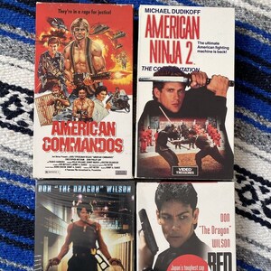 May include: Four VHS movie tapes are displayed, featuring action film titles like "American Commandos," "American Ninja 2," "Terminal Rush," and "Red Sun Rising." Each tape has colorful cover art with action scenes and text.