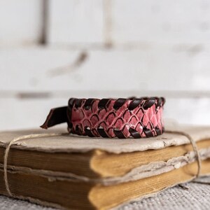Peut inclure: Un bracelet en cuir rose et marron avec un design tressé posé sur deux vieux livres usés.