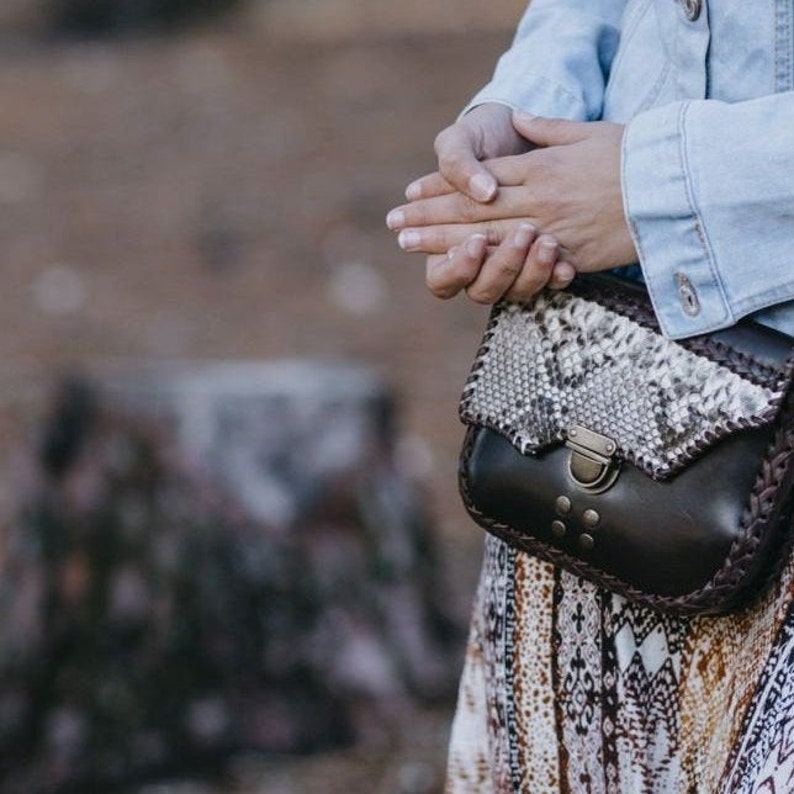 May include: A small brown leather purse with a snakeskin flap and a silver clasp. The purse has a braided strap and is worn over the shoulder.