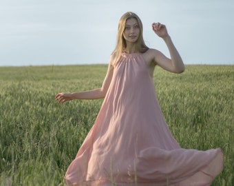 Puede incluir: Una mujer con un vestido rosa camina por un campo de hierba verde alta.