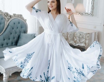 Puede incluir: Un vestido cruzado blanco de largo midi con escote en V, mangas cortas y un lazo a juego en la cintura. El dobladillo y las mangas están decorados con un estampado botánico azul de hojas y ramas, creando una silueta fluida y falda acampanada.