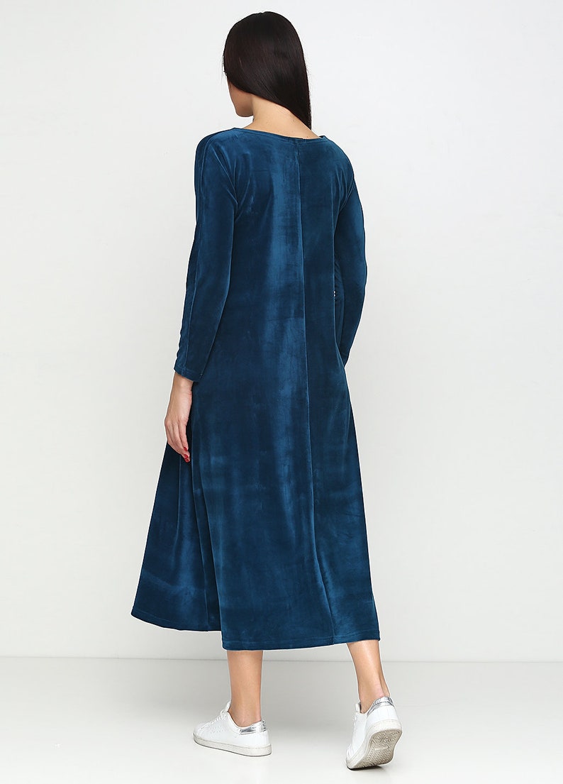 May include: A long-sleeved, teal blue velvet dress with a round neckline. The dress has a slightly flared skirt and is shown on a model wearing white sneakers.