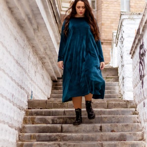 May include: A woman wearing a teal blue velvet dress and black combat boots walks down a set of concrete stairs.