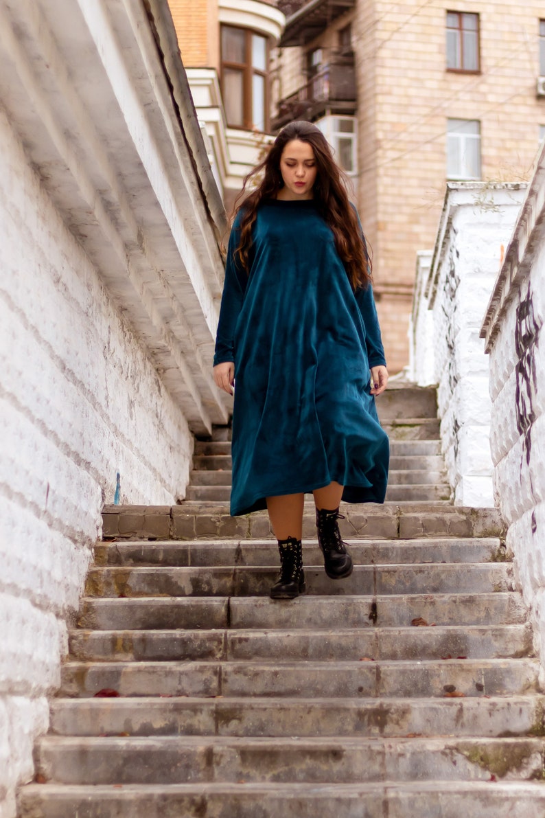May include: A woman wearing a teal blue velvet dress and black combat boots walks down a set of concrete stairs.