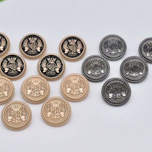 May include: A collection of gold and silver metal buttons with a crest design. The buttons have a raised edge and a black or gold coloured crest with a crown on top.