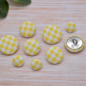 May include: Assortment of yellow and white gingham fabric buttons with a silver shank button.