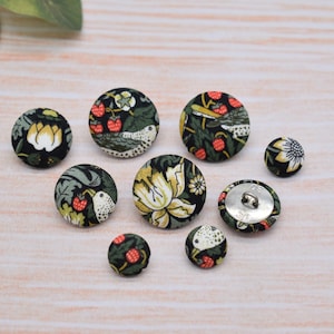 May include: Assortment of eight fabric covered buttons with a floral and bird design. The buttons are in shades of green, black, white, and red.