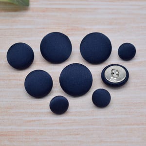 May include: A set of eight navy blue buttons, some with a silver shank and some with a flat back.