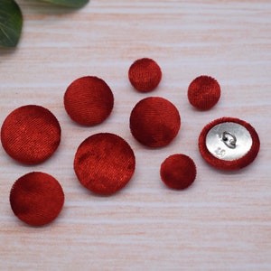 Puede incluir: Surtido de diez botones de terciopelo rojo en varios tamaños. Los botones son redondos y tienen una textura suave y aterciopelada.