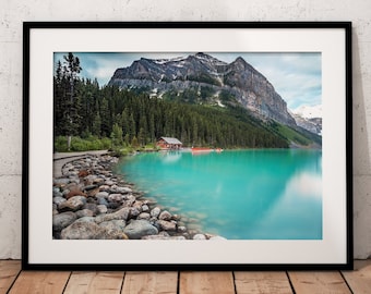 May include: A framed photograph of a mountain lake with a small cabin on the shore. The water is a vibrant turquoise blue and the mountains are covered in trees.