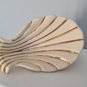 Può includere: Un piatto in ceramica bianca a forma di conchiglia con dettagli dorati. Il piatto ha la forma di una conchiglia e una finitura liscia e lucida.