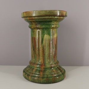 May include: A ceramic pedestal with a green, brown, and yellow glaze. The pedestal has a round top and a fluted column.
