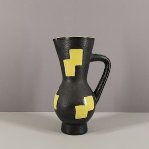 May include: A black ceramic vase with a yellow geometric pattern. The vase has a wide base and a narrow neck with a handle.