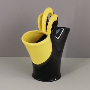 May include: A black and yellow ceramic vase with a unique handle design. The vase is glazed and has a smooth finish.