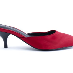 May include: Red satin heeled mules with a pointed toe and a low heel. The shoes have a black sole and a black leather insole.