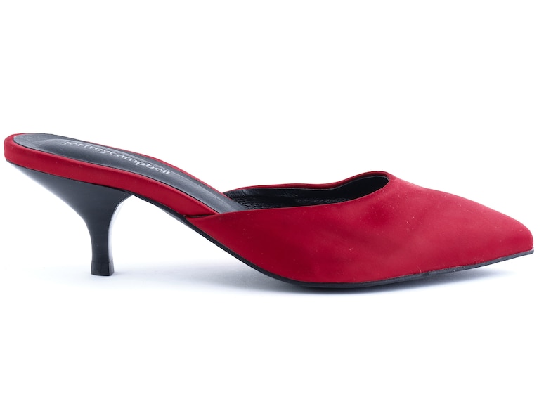 May include: Red satin heeled mules with a pointed toe and a low heel. The shoes have a black sole and a black leather insole.