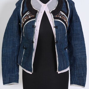 May include: A blue denim jacket with a black and white trim and beaded embellishments. The jacket has a button closure and long sleeves.