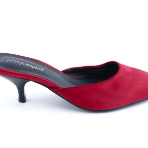 May include: Red satin heeled mule with a pointed toe and a low heel. The shoe has a black insole with the text "jeffreycampbell" printed on it.
