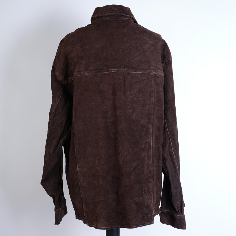 Puede incluir: Una camisa de manga larga de ante marr&oacute;n con cuello abotonado y un bolsillo en el pecho.
