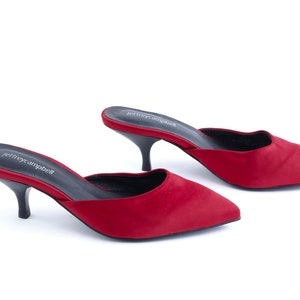 May include: A pair of red satin heeled mules with a pointed toe. The shoes have a black heel and the brand name "jeffreycampbell" is printed on the insole.