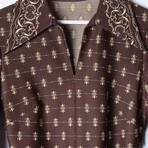 Può includere: Una camicia marrone con colletto e un motivo a fantasia con un motivo geometrico ripetitivo e un bordo dorato e marrone intorno al colletto.