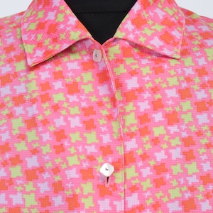 Può includere: Una camicia rosa con bottoni e un motivo geometrico verde e arancione. La camicia ha un colletto e due bottoni.