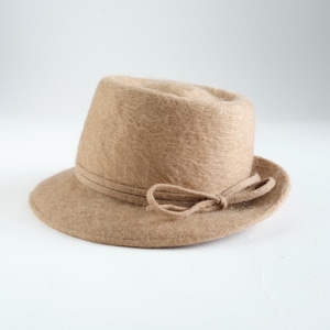May include: A tan-coloured fedora hat with a small brim and a decorative bow. The hat has a soft, textured appearance and a band around the crown. This stylish hat is suitable for various occasions.