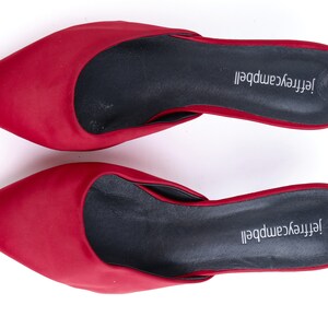 May include: A pair of red satin heeled mules with black insoles. The insoles are labeled "Jeffrey Campbell".