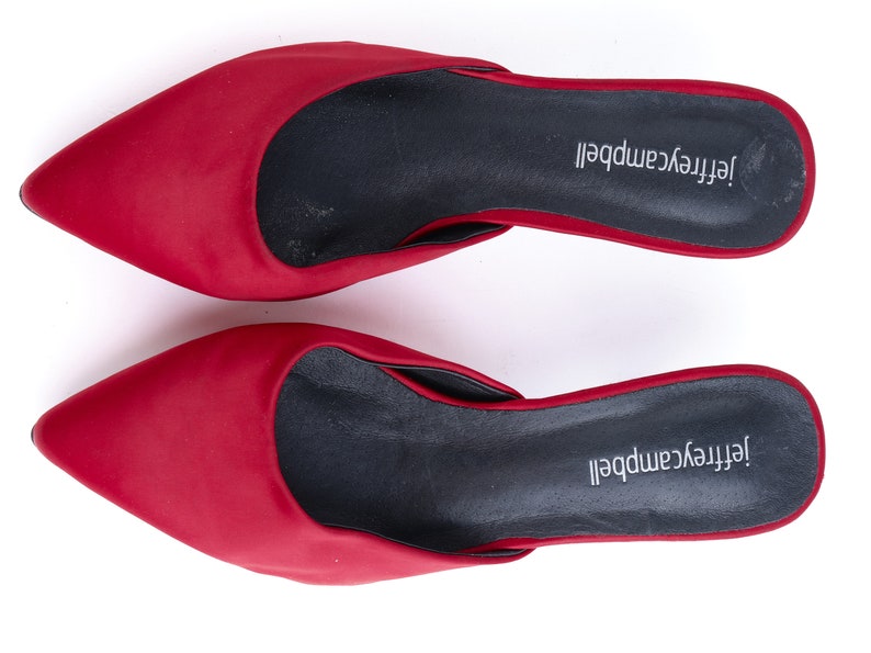 May include: A pair of red satin heeled mules with black insoles. The insoles are labeled "Jeffrey Campbell".