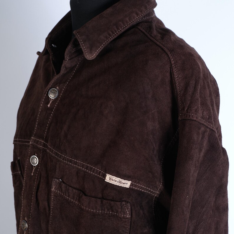 Puede incluir: Una chaqueta de ante marr&oacute;n con cierre de botones y un bolsillo en el pecho. La chaqueta tiene una etiqueta que dice "Wrangler".