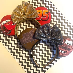 May include: A selection of character headbands inspired by the Cars movie. The headbands feature gold and black sequin bows, and round accents with Lightning McQueen, Tow Mater, and the number 95. The headbands have black and gold trim.