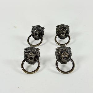 May include: Four antique bronze lion head drawer pulls with ring handles. The lion heads have detailed manes and open mouths. The ring handles are attached to the lion's mouth.